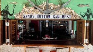 A bar area with a sign reading "SANDY BOTTOM BAR REST" above a counter with two stools. - SEA FRONT-Private, natural, couples-only...unique paradise focused on peace (Banda Abou)