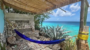 A beachside structure with a stone wall, a blue hammock, and a view of the ocean. - SEA FRONT-Private, natural, couples-only...unique paradise focused on peace (Banda Abou)