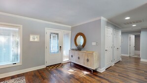 Een ruime hal met houten vloeren, een witte console tafel met spiegel, en een deur naar een andere kamer.