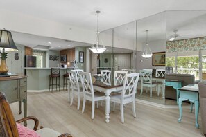 Una cocina amplia con comedor, que cuenta con una isla central, sillas blancas e iluminación colgante.