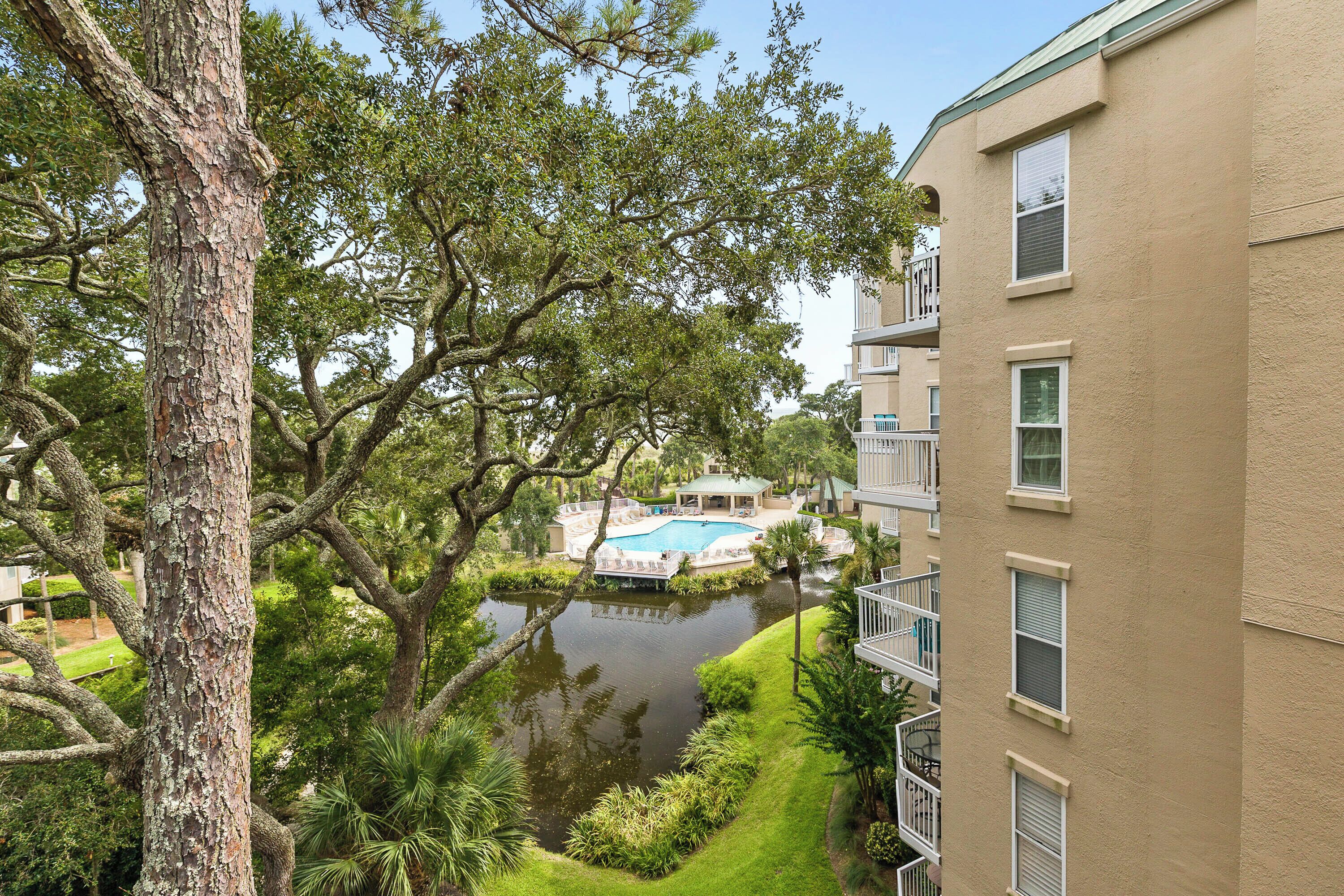 A residential building with a swimming pool surrounded by trees and a small pond.