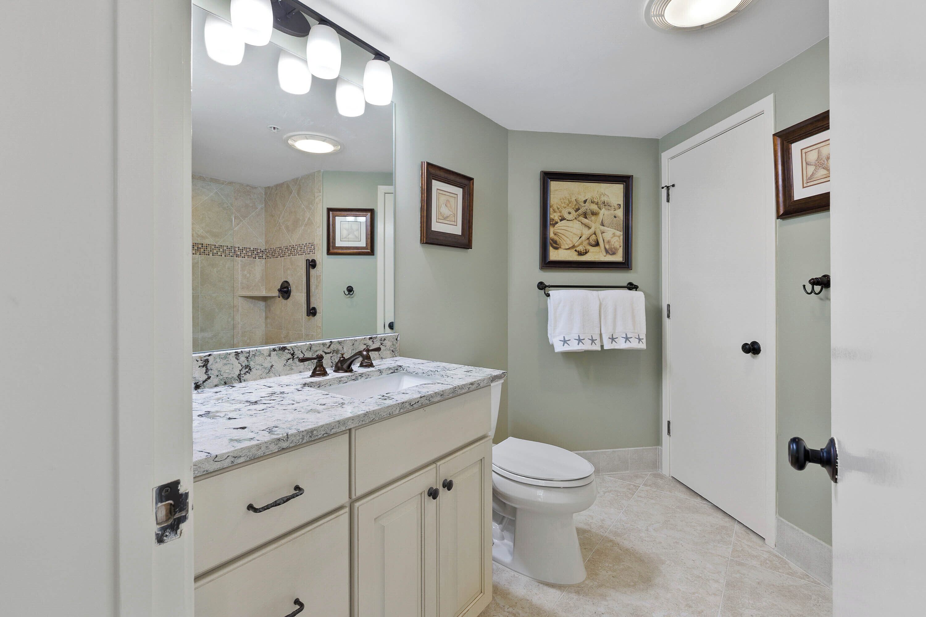 A bathroom with a marble sink, a toilet, and a door with a towel hanging on the wall.