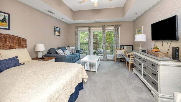 A bedroom with a bed, a sofa, a TV, a dresser, and a ceiling fan. - Located just blocks from Oceanfront Neptune Park (Saint Simons Island)