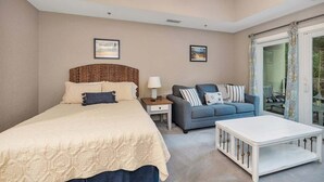 A bedroom with a bed, a nightstand, a sofa, a coffee table, and a large window with curtains. - Located just blocks from Oceanfront Neptune Park (Saint Simons Island)