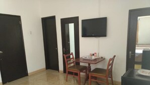 A room with a dining table, two chairs, a television mounted on the wall, and a door. - Lasa Residence (Oranjestad)