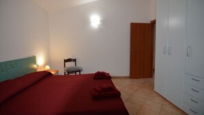 Un dormitorio con cama, una silla, un armario y una mesita de noche con lámpara.
