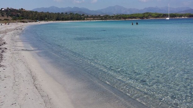 Una playa con agua turquesa cristalina, una orilla de arena y montañas a lo lejos.