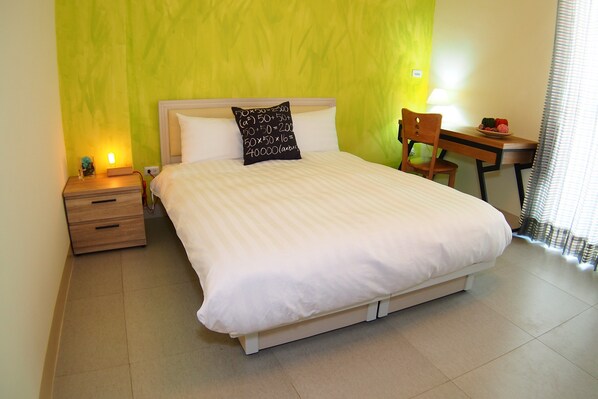 A neatly made bed with a pillow, a bedside table with a lamp, and a chair at a desk with a fruit bowl. - Ruisui 38 Homestay (Ruisui)
