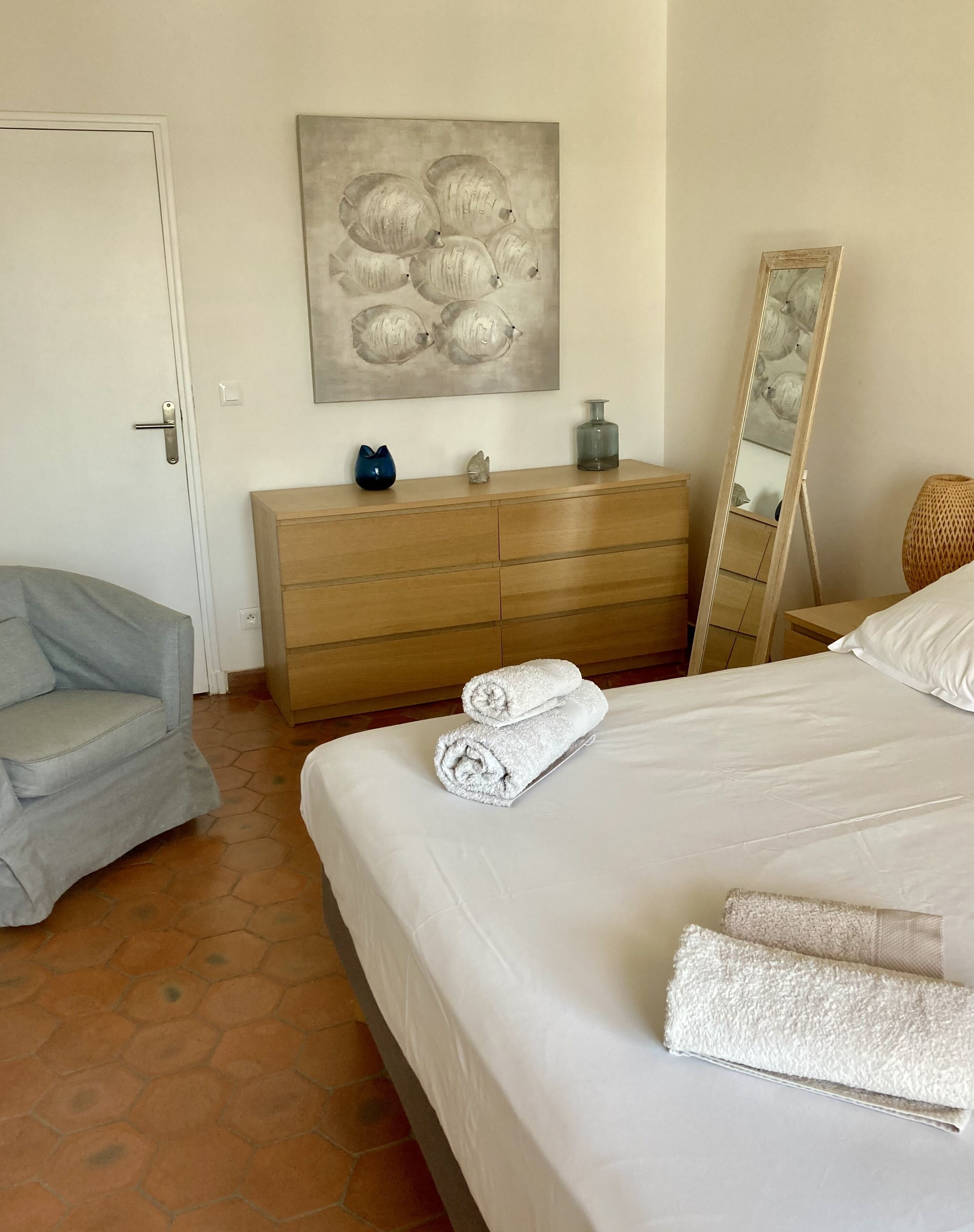 Un dormitorio con una cama, un aparador de madera, una silla, un cuadro y un espejo.
