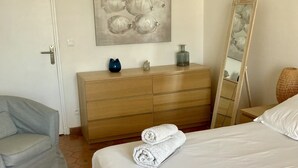 Une chambre à coucher avec un lit, une commode en bois, une chaise, un tableau et un miroir.