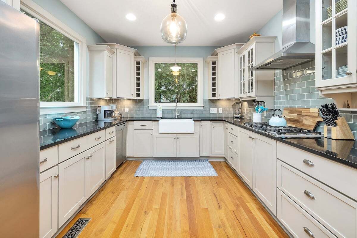 A modern kitchen with white cabinets, a black countertop, and a wooden floor.