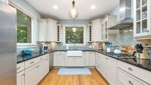 Una cocina moderna con armarios blancos, encimera negra y suelo de madera.