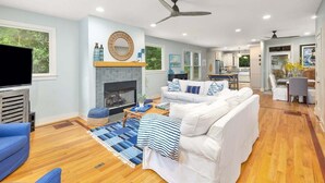Una sala de estar moderna con chimenea, un sofá blanco, un sillón azul y un televisor de pantalla plana.