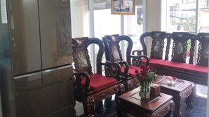A room with a refrigerator, wooden chairs with red cushions, a table with a vase of flowers, and a ceiling fan. - Thanh Vinh Hotel (Ho Chi Minh City)