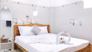 A neatly made bed with white linens and a wooden headboard, a towel rack with towels, and a sign indicating no smoking. - Thanh Vinh Hotel (Ho Chi Minh City)