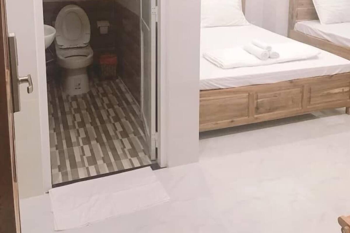 Une chambre d’hôtel avec un lit en bois, une salle de bain blanche avec des toilettes et un espace douche.