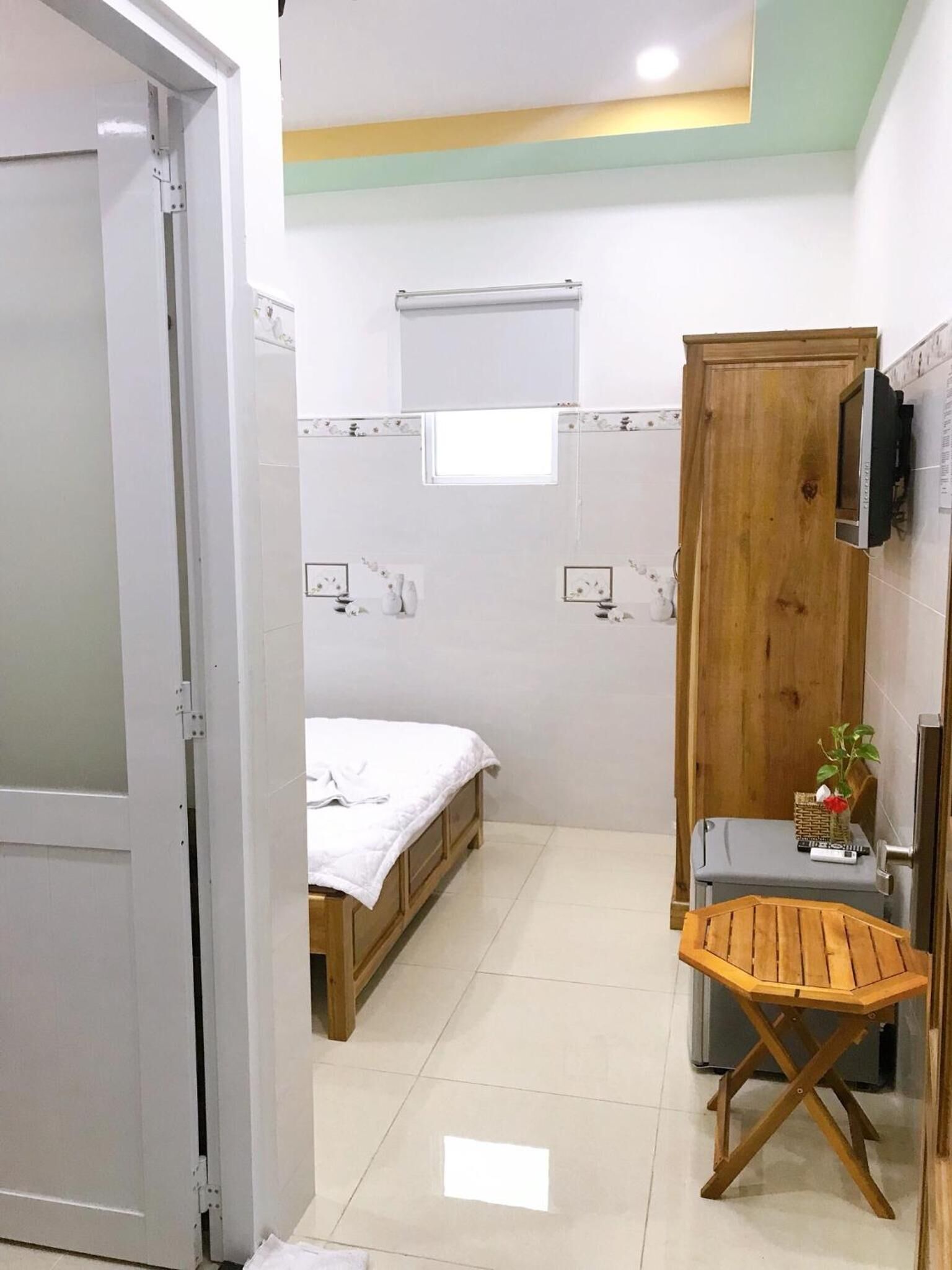 A compact room with a bed, a small table, a TV mounted on the wall, and a wooden door.
