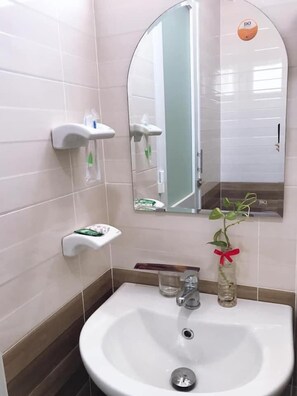 A bathroom with a white sink, a mirror, and a glass shower enclosure. - Thanh Vinh Hotel (Ho Chi Minh City)