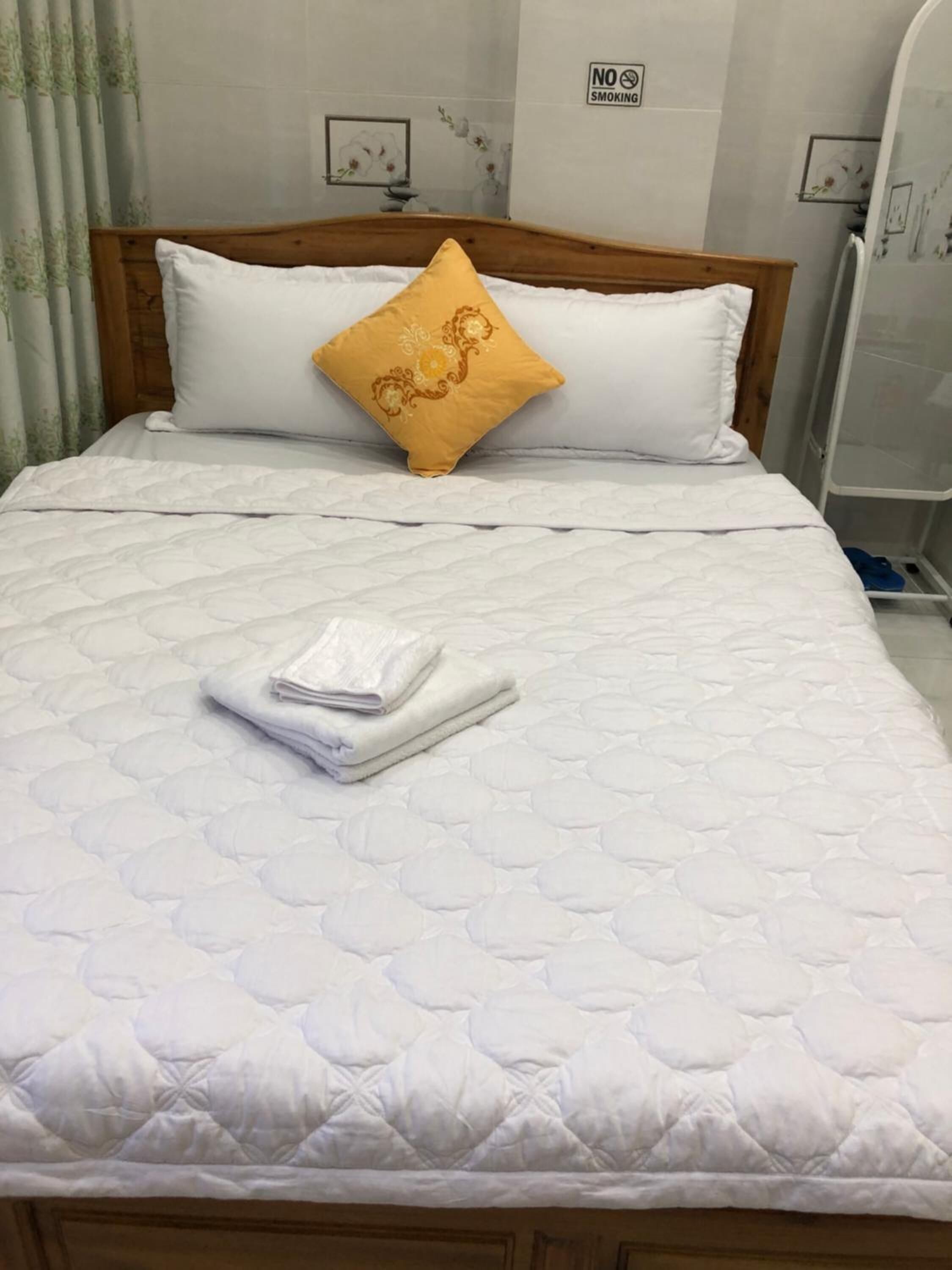 A neatly made bed with a white quilted mattress, a wooden headboard, and a single decorative pillow.