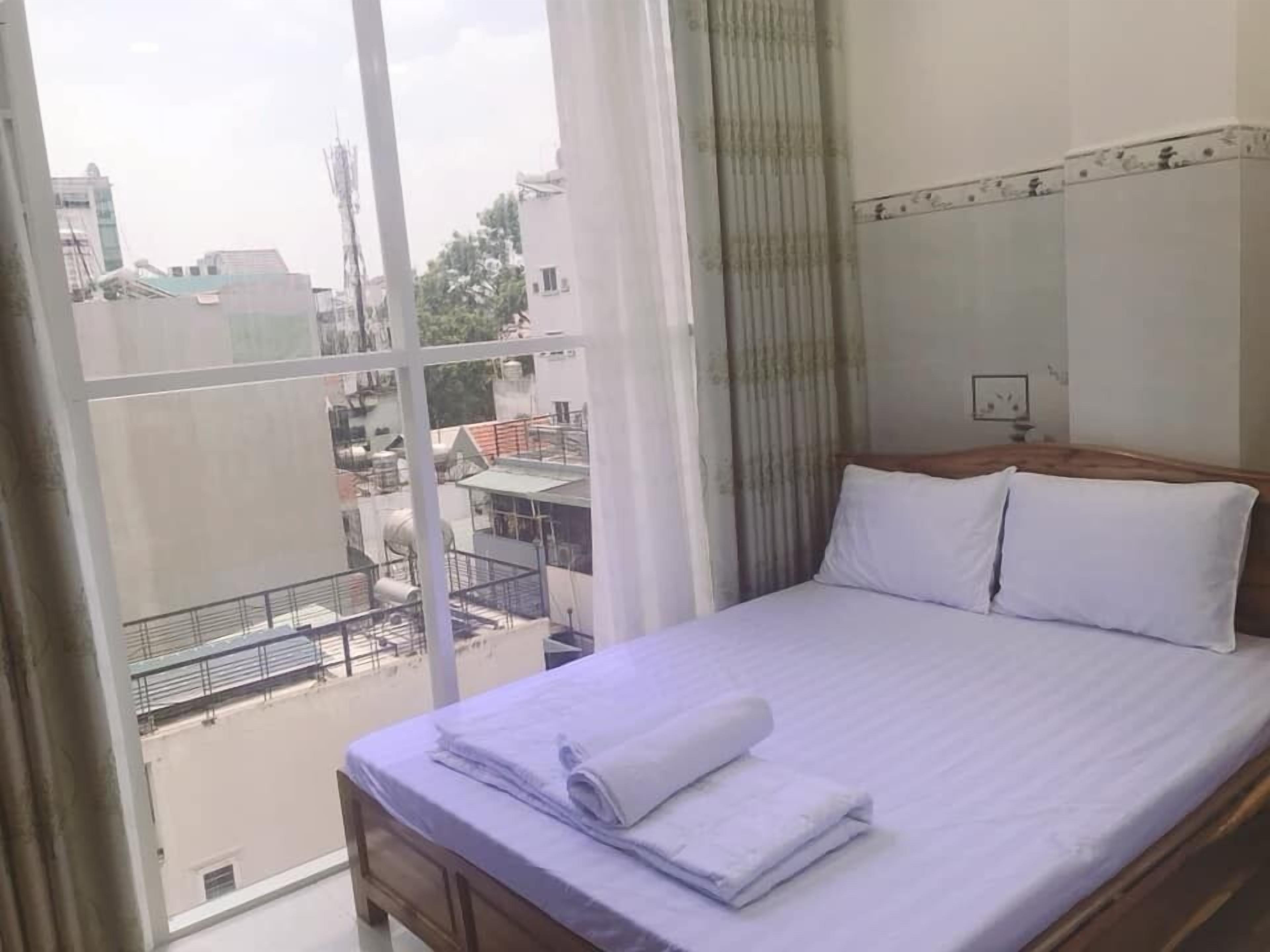 A hotel room with a large window, a bed with white linens, and a view of buildings outside.