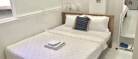 A neatly made bed with a quilted mattress, a folded towel, and a decorative pillow.
