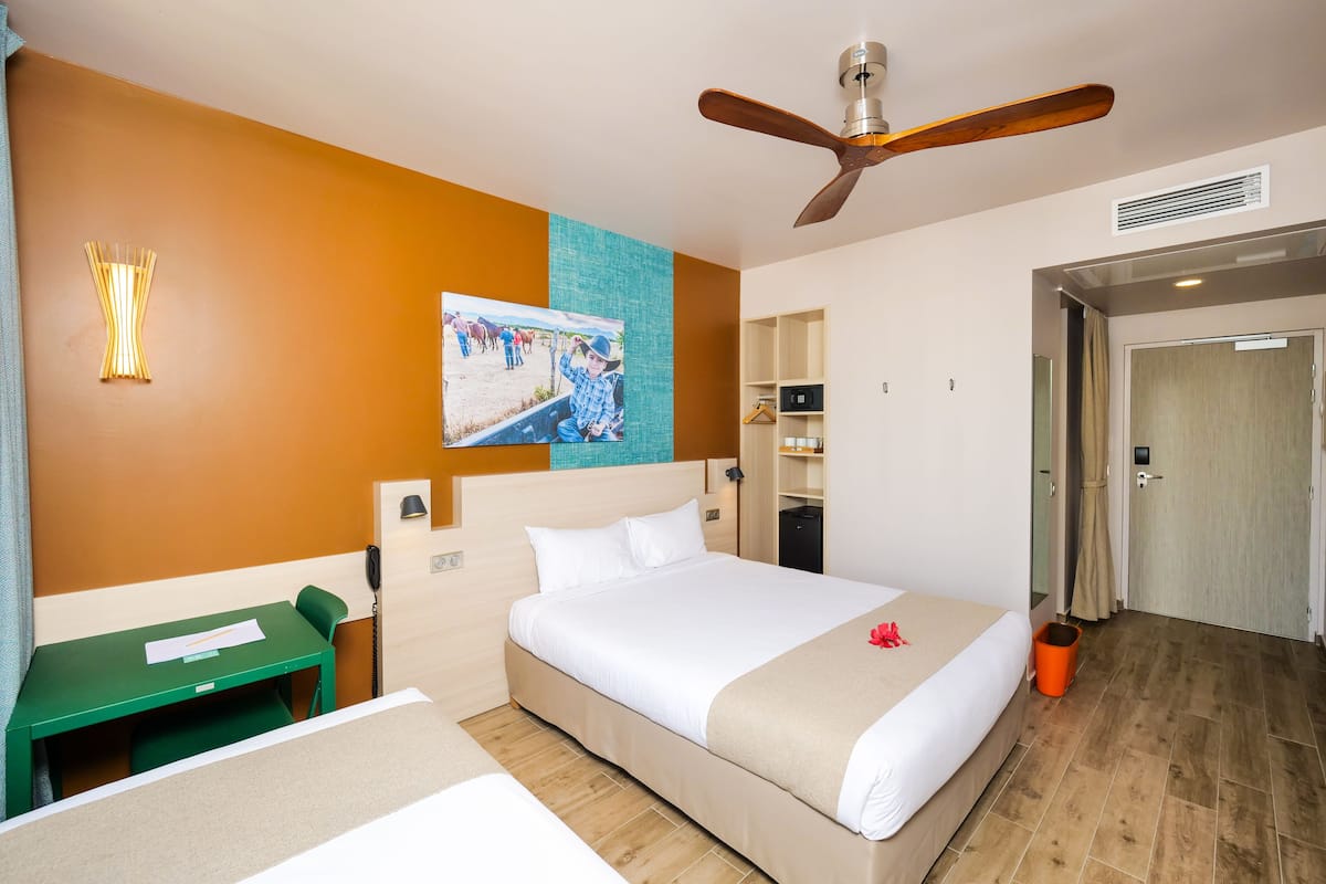 A hotel room with a large bed, a desk, a ceiling fan, and a painting on the wall.