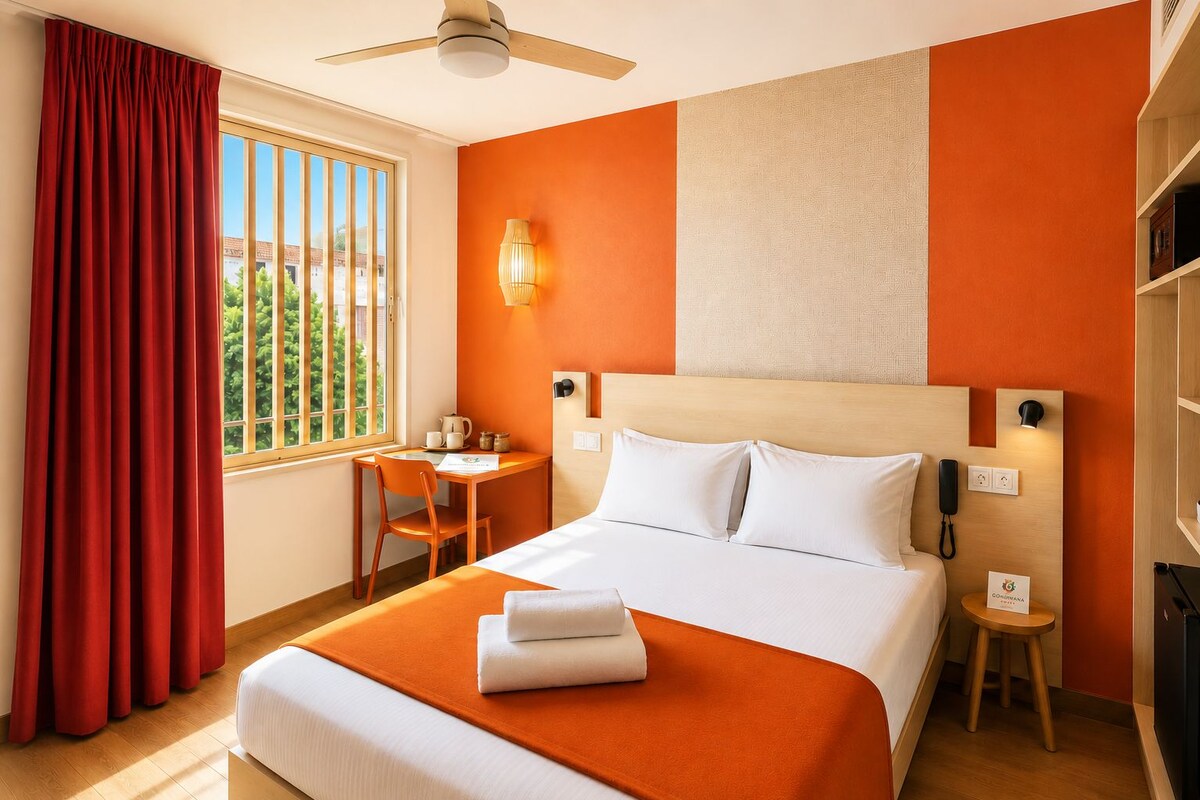 A hotel room with a bed, a desk, a chair, a window with curtains, a ceiling fan, and a wall-mounted lamp.
