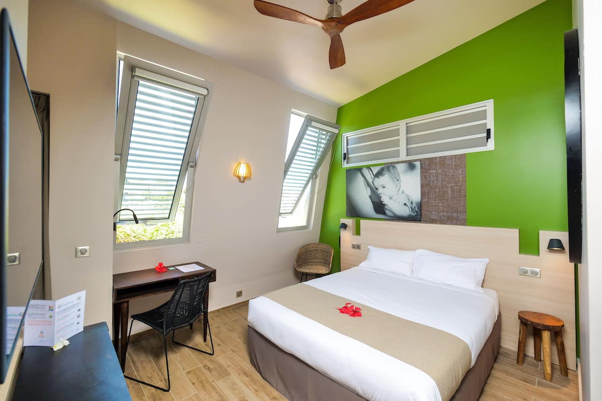 A hotel room with a bed, desk, chair, and a ceiling fan.