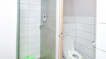 A modern bathroom with a glass shower enclosure, a toilet with a green seat, and a small green stool.