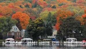 Vista a un lago con barcos amarrados, un pabellón y casas al fondo.