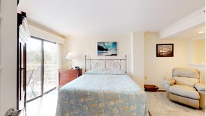 Una camera da letto con un letto, una sedia, un comodino, una lampada e un quadro appeso al muro.