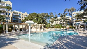 A hotel pool area with multiple lounge chairs, a covered seating area, and a clear blue pool.