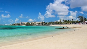 Une plage à l’eau turquoise et limpide, un navire de croisière à l’horizon et une rangée de bâtiments le long de la côte.