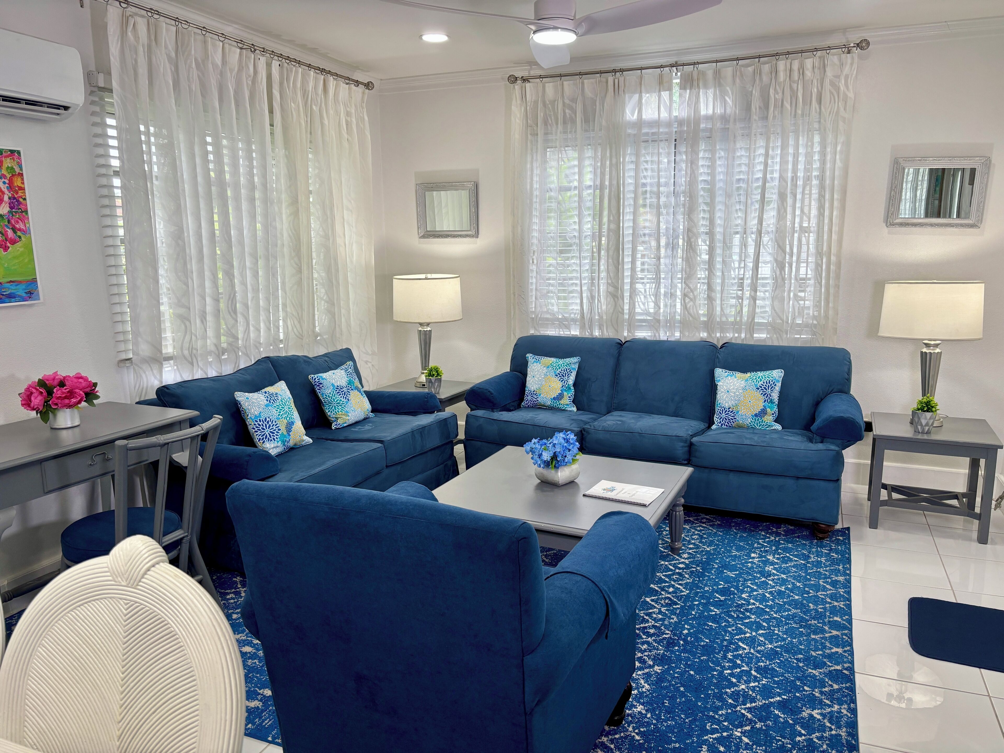 Ein modernes Wohnzimmer mit einem blauen Sofagarnitur, einem Couchtisch und einem Essbereich mit einem kleinen Tisch und Stühlen.