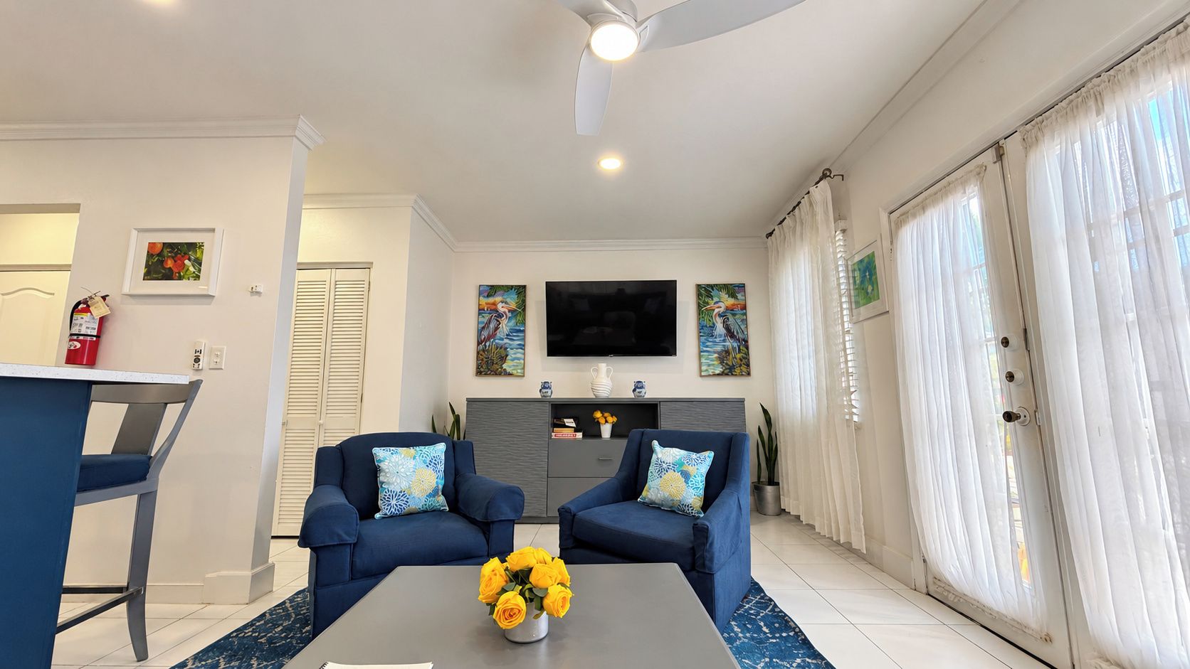 A living room with two sofas, a coffee table with flowers, a TV, and a sliding glass door.