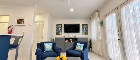 A living room with two sofas, a coffee table with flowers, a TV, and a sliding glass door.