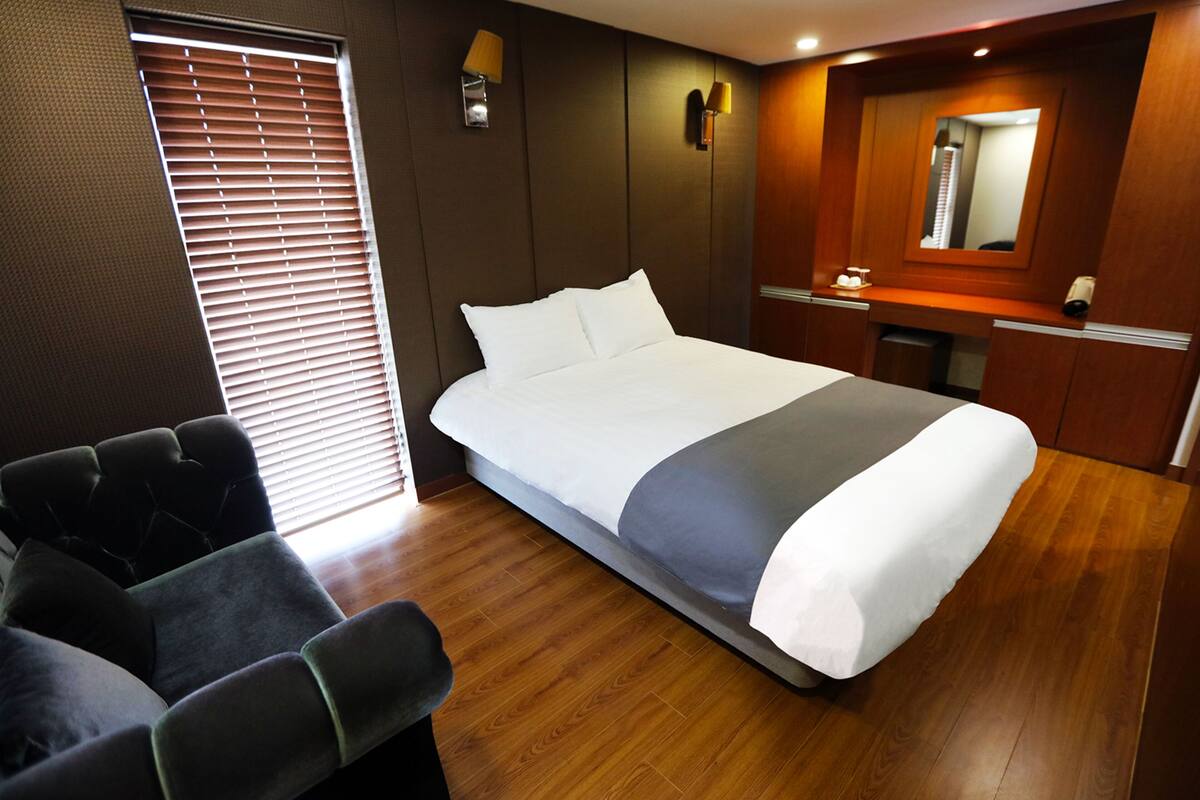 A hotel room with a large bed, a seating area, a vanity with a mirror, and a window with blinds.