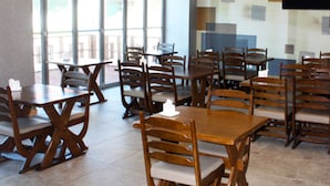 Un espace repas avec des tables et des chaises en bois, de grandes fenêtres et un téléviseur à écran plat fixé au mur.