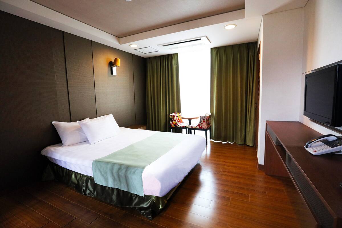 A hotel room with a large bed, a desk with a telephone, a television, and a chair.