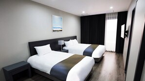 Une chambre d’hôtel avec deux lits, une table de chevet, une lampe, un tableau au mur et une fenêtre avec des rideaux.