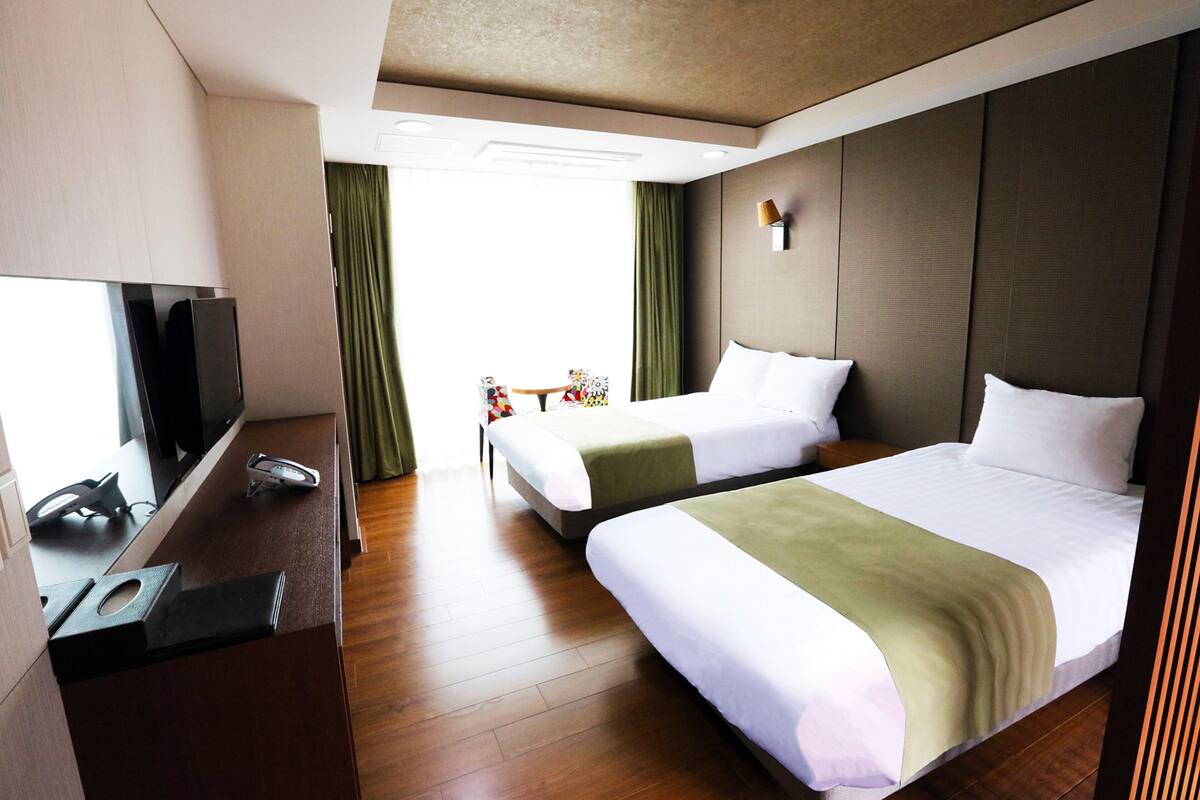 A hotel room with two beds, a desk with a television, and a small table with a telephone.