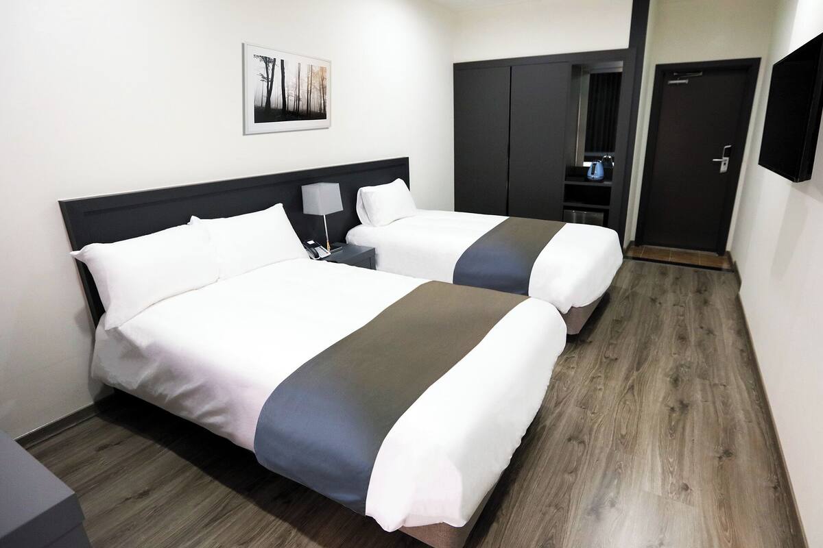 A hotel room with two beds, a wardrobe, a desk, and a coffee machine.