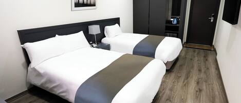 Habitación de hotel con dos camas, un armario, un escritorio y una cafetera.