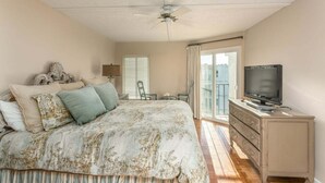 A bedroom with a bed, a television on a dresser, and a balcony with a view. - Oceanview unit at The Beach Club.  Pool, Great Bea (Saint Simons Island)