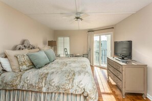 A bedroom with a bed, a television on a dresser, and a balcony with a view. - Oceanview unit at The Beach Club.  Pool, Great Bea (Saint Simons Island)