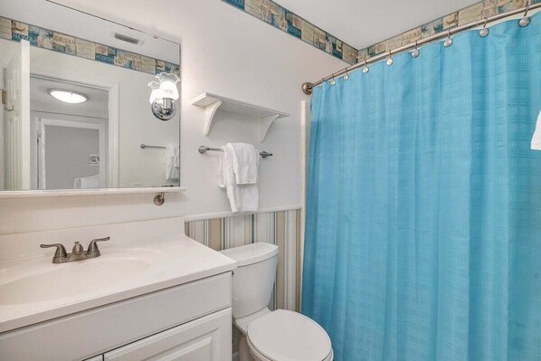 A bathroom with a white sink, a mirror, a towel rack, and a blue shower curtain. - Oceanfront Condo with Balcony, Pool, Beach Access (Saint Simons Island)