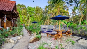 A tropical garden with a stone pathway, lounge chairs, and umbrellas. - Asoka Bungalows (Penida Island)