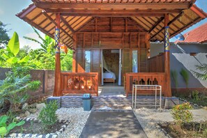 A wooden structure with a covered entrance, a bed, and a small outdoor seating area. - Asoka Bungalows (Penida Island)