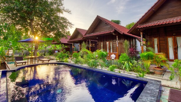 A pool area with wooden cabins, surrounded by lush greenery and a clear sky. - Asoka Bungalows (Penida Island)