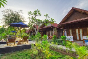 A wooden villa with a garden patio, outdoor seating, and a red-tiled roof. - Asoka Bungalows (Penida Island)